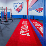 This gym boasts a professional design with mirrored walls, bright blue and red color schemes, and a central training area equipped with weight racks and bars. The red turf, emblazoned with "Collège Français" in bold white text, provides an energizing and customized training surface for athletes.