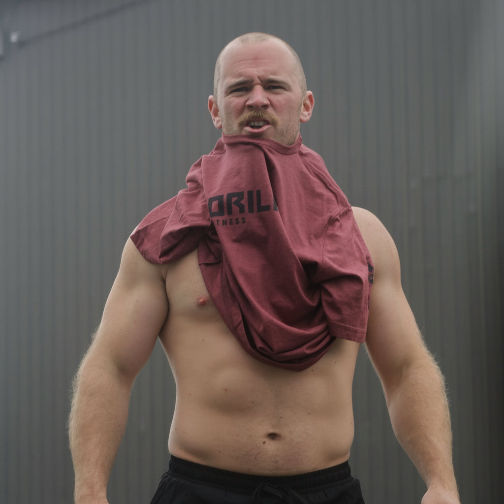 Man with a red workout tee draped over his shoulder against a gray background